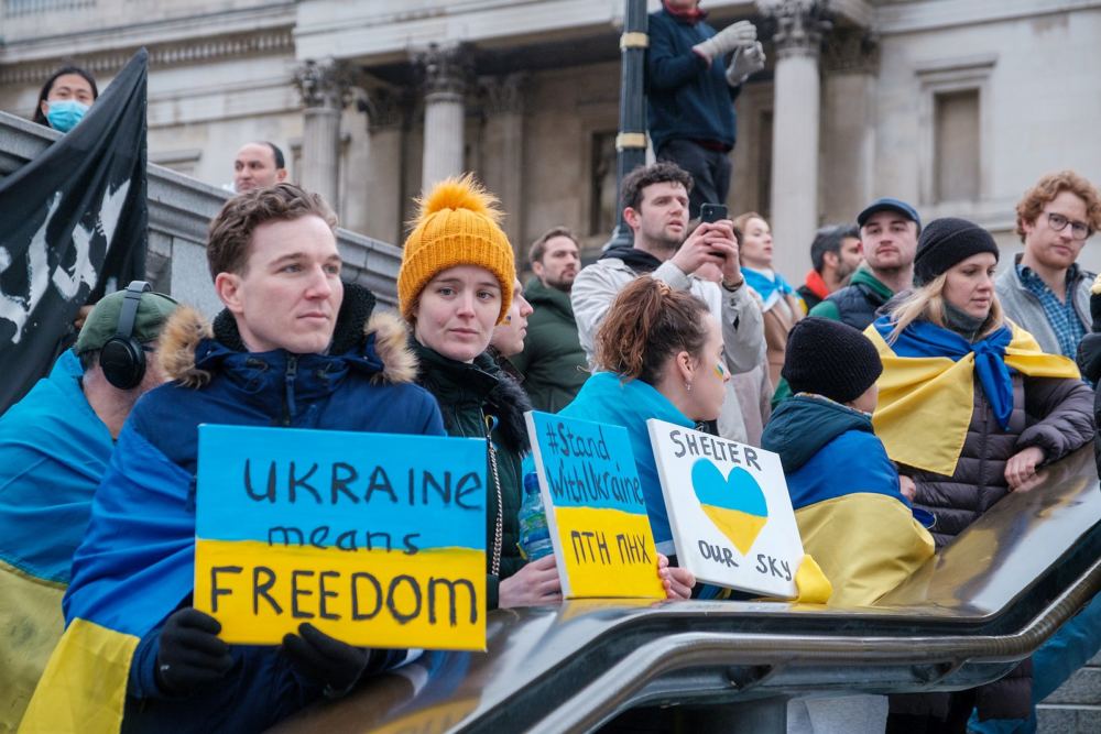 Menschen auf Demonstration mit Schildern in den ukrainischen Farben.