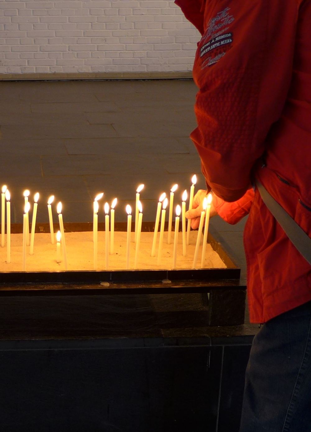 Person zündet eine Kerze im Kerzenbecken an